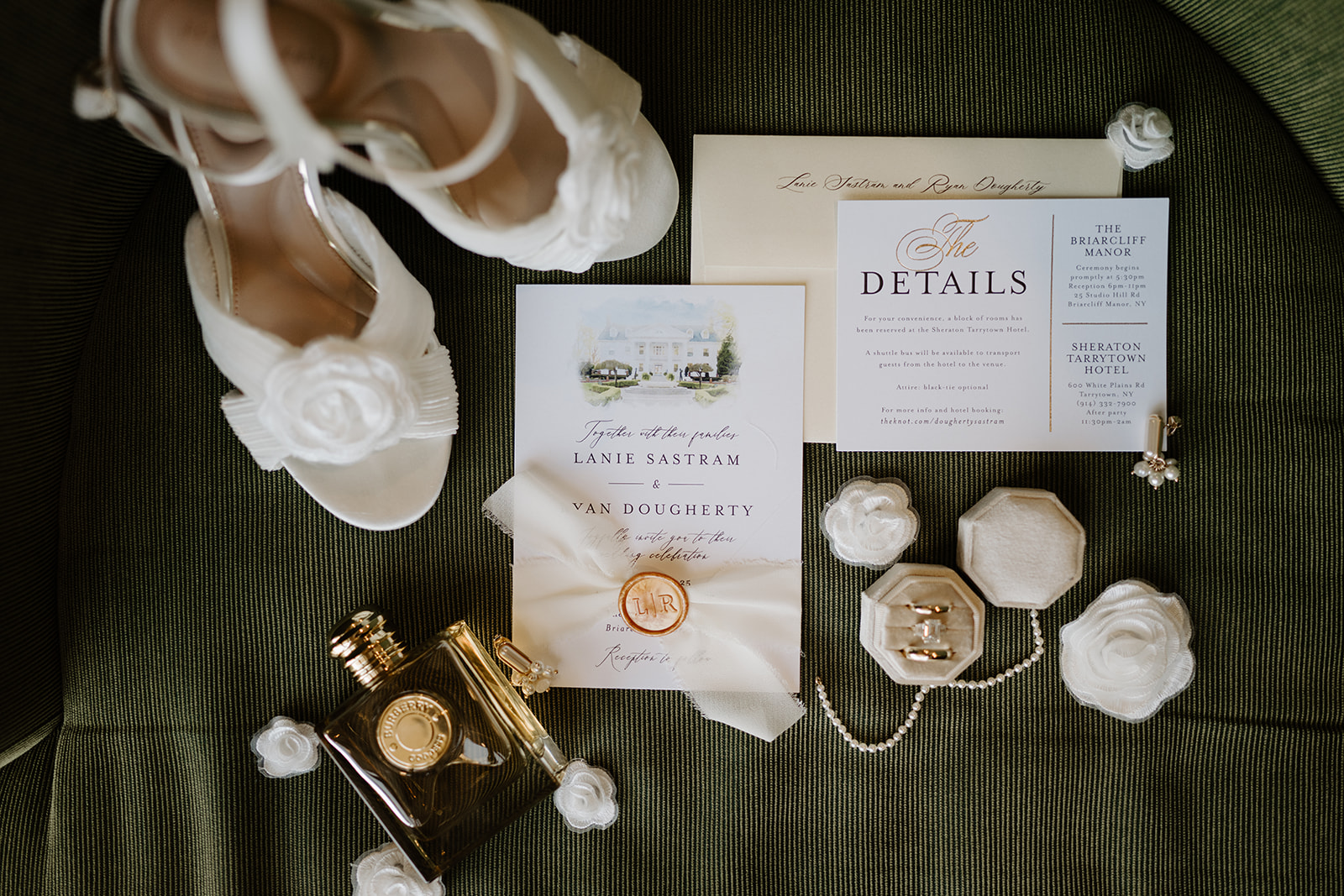 Flat lay of wedding details, featuring white shoes, invitations with a wax seal, perfume, and rings.